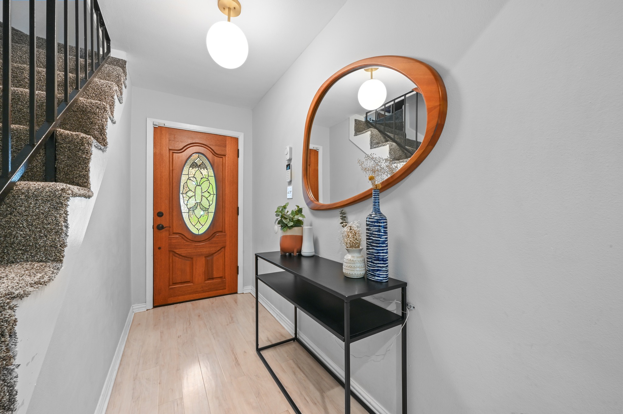 2509 Redleaf Lane Austin, TX 78745 - Photo 5 of 28 Entryway featuring light wood-finish flooring, a detailed wood entry door with an oval stained-glass insert, and a carpeted staircase with dark metal railings