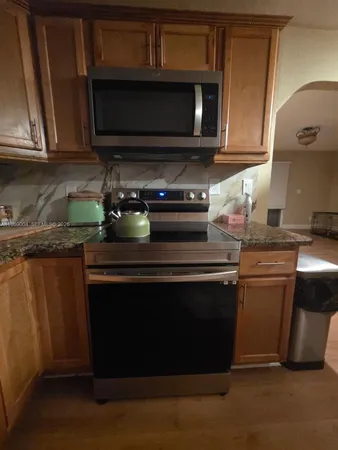 a kitchen with granite countertop a stove top oven microwave and cabinets