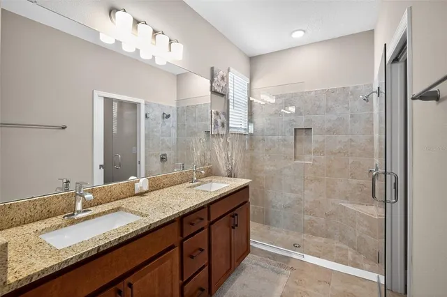 a bathroom with a granite countertop double vanity sink mirror and shower