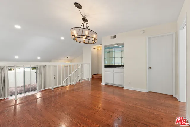 a view of empty room with wooden floor and kitchen