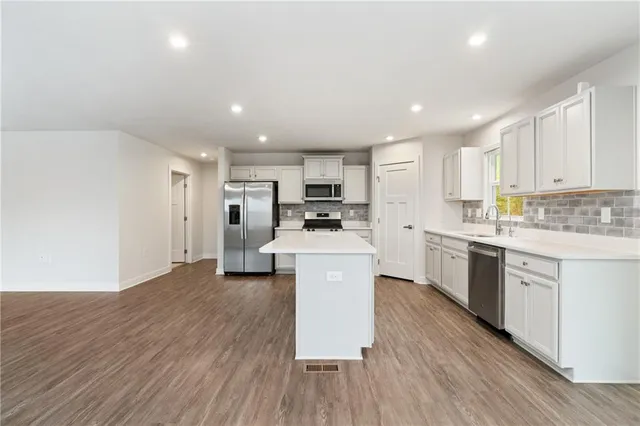 a kitchen with stainless steel appliances kitchen island granite countertop a stove a sink a refrigerator and white cabinets with wooden floor