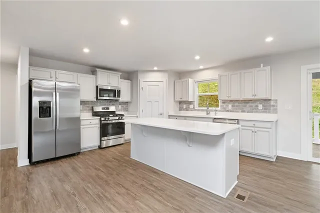 a kitchen with stainless steel appliances granite countertop a refrigerator a sink dishwasher a stove and white cabinets with wooden floor