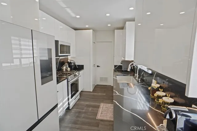 a kitchen with stainless steel appliances kitchen island granite countertop a refrigerator a stove and a sink with wooden floor