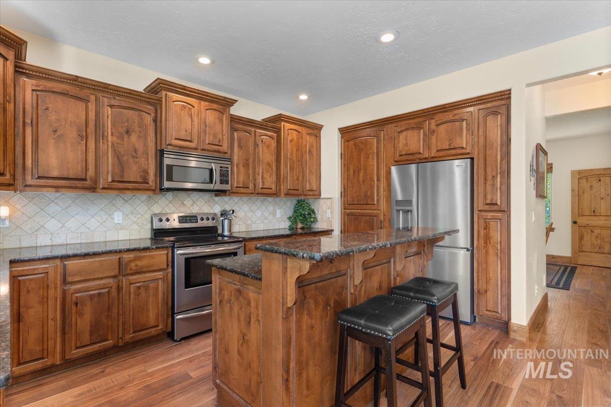 4154 North Tipton Avenue Meridian, ID 83646 - Photo 12 of 50 Well-appointed kitchen featuring wood cabinetry, stainless steel appliances, a tiled backsplash, and granite-style countertops