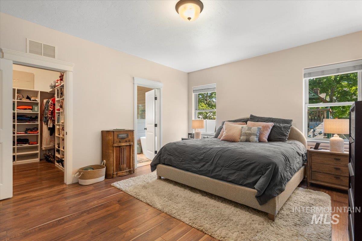4154 North Tipton Avenue Meridian, ID 83646 - Photo 21 of 50 Bedroom featuring rich wood-finish flooring, a built-in closet organization system, two windows, a ceiling-mounted light fixture, and a doorway opening to a bathroom with a visible bathtub