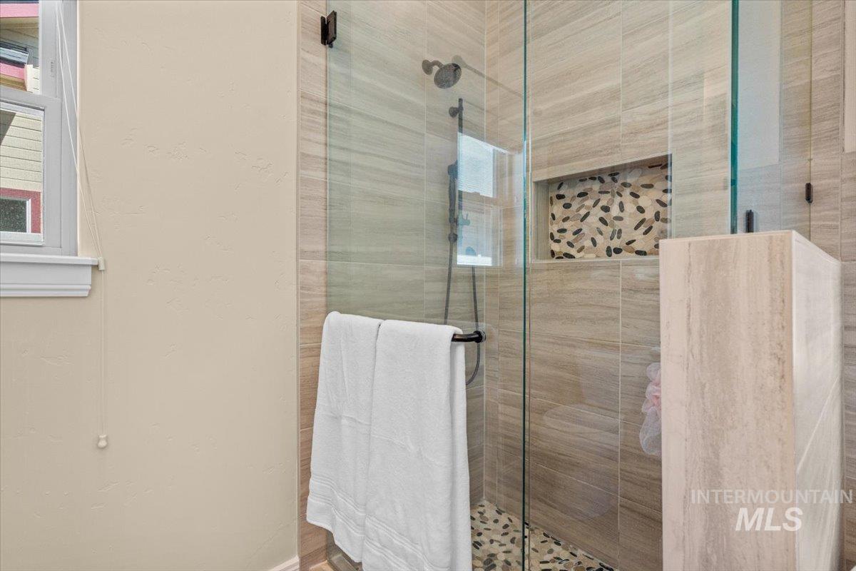 4154 North Tipton Avenue Meridian, ID 83646 - Photo 27 of 50 Glass-enclosed shower with a rainfall showerhead, stone-finish wall tiling, pebble-finish flooring, and a built-in tiled niche