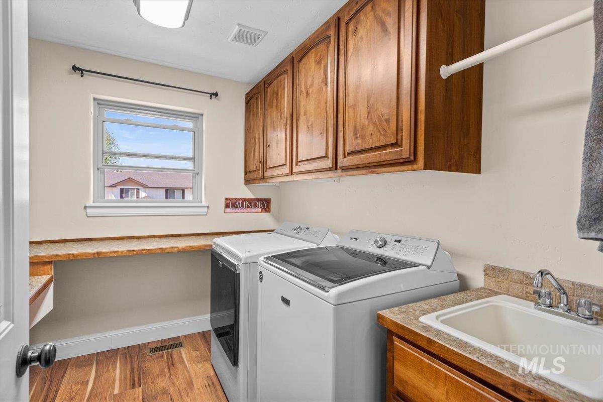 4154 North Tipton Avenue Meridian, ID 83646 - Photo 43 of 50 Laundry area featuring wood-finish flooring, a window, wood cabinetry, a utility sink with a tiled backsplash, and a clothes hanging rod