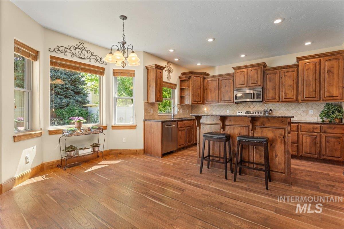 4154 North Tipton Avenue Meridian, ID 83646 - Photo 9 of 50 Kitchen featuring wood-finish flooring, custom wood cabinetry, stainless steel appliances, and a central island with bar seating
