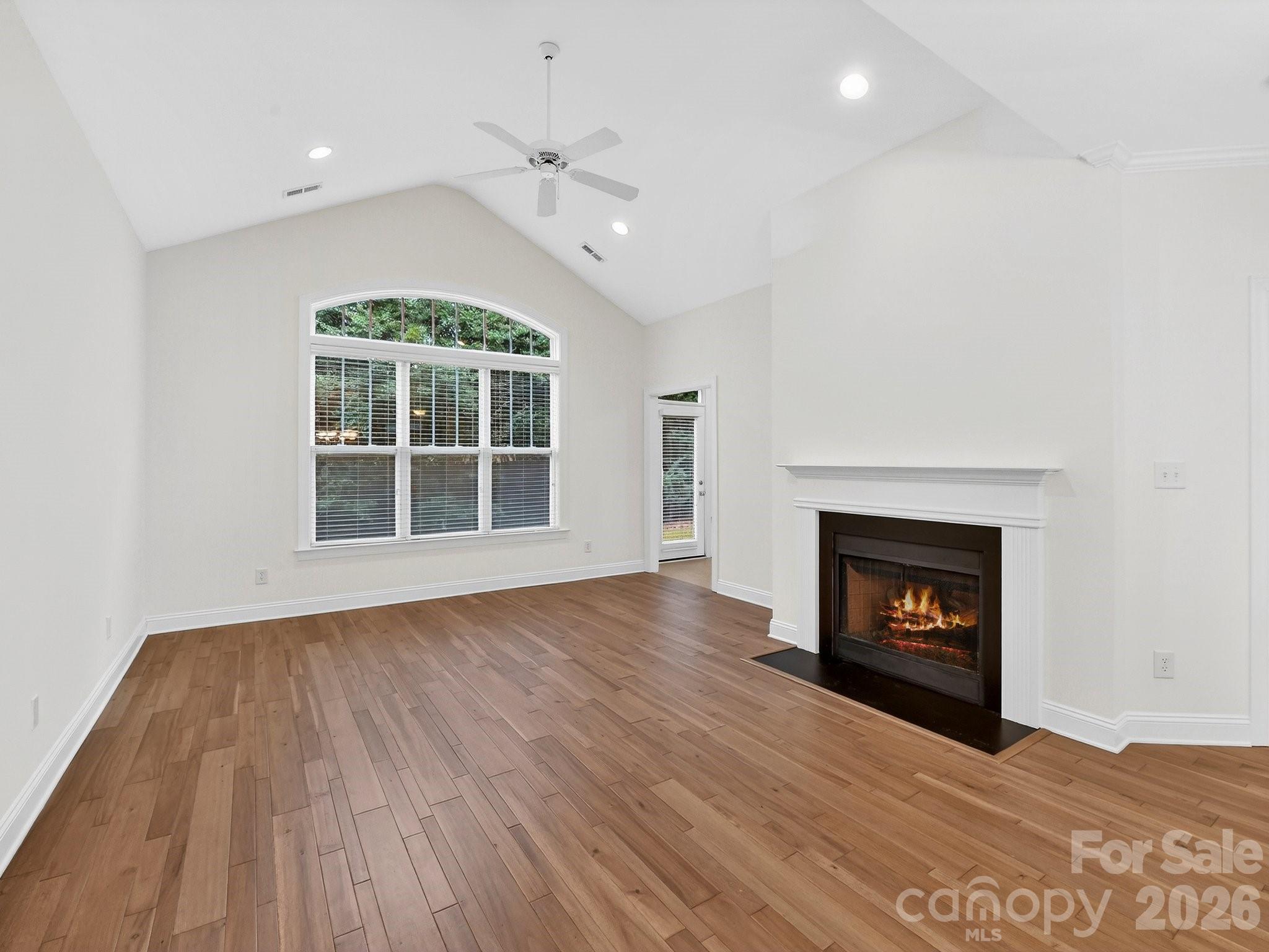 2963 Bellasera Way Matthews, NC 28105 - Photo 3 of 45 an empty room with wooden floor fireplace cabinet and windows