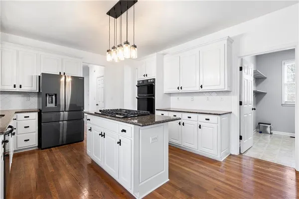 a kitchen with stainless steel appliances a stove a refrigerator a chimney a sink cabinets and wooden floor