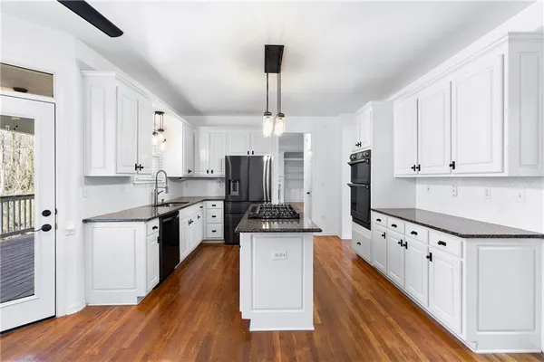 a kitchen with granite countertop a refrigerator a stove a sink dishwasher and white cabinets with wooden floor