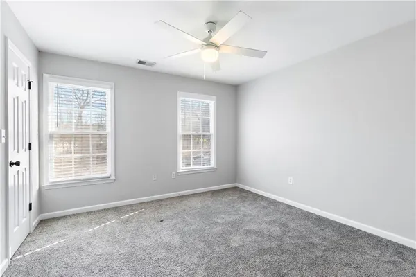 an empty room with chandelier fan and windows