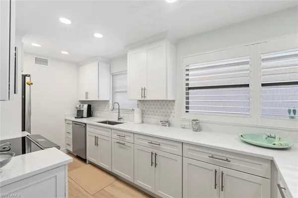 a kitchen with a sink dishwasher a stove and white cabinets with wooden floor