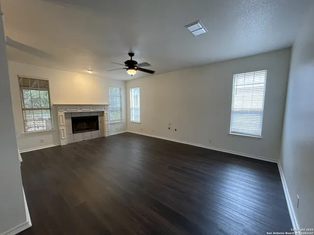 an empty room with wooden floor fireplace and windows
