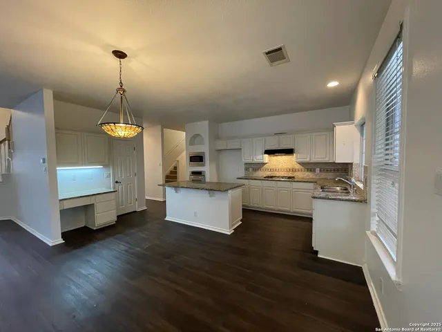 a kitchen with stainless steel appliances kitchen island granite countertop a stove a sink a refrigerator and white cabinets with wooden floor