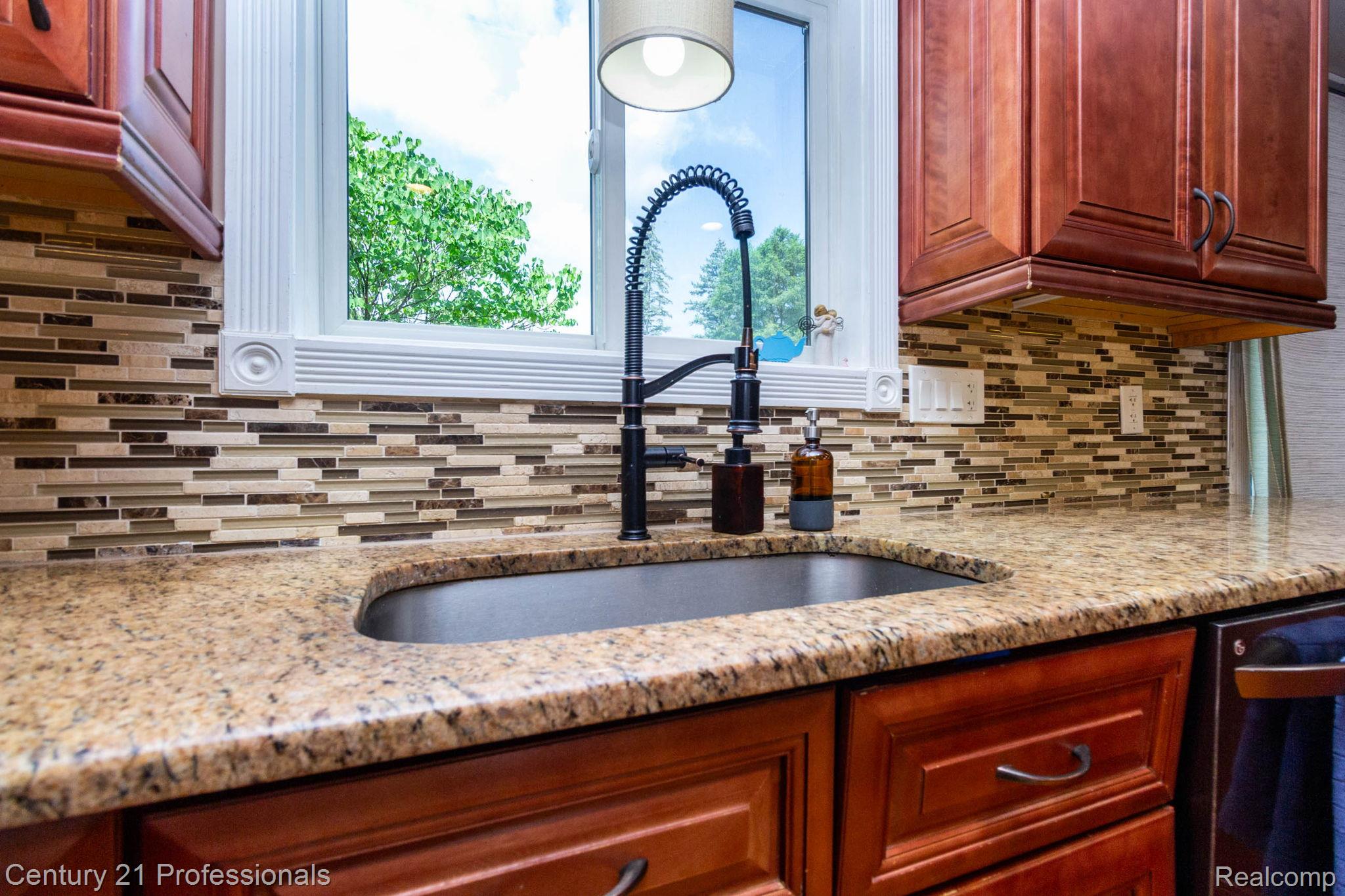 671 Bridgestone Drive Rochester, MI 48309 - Photo 14 of 50 Kitchen workstation featuring a black composite sink with a matte black high-arc faucet, granite countertops, and a mosaic tile backsplash