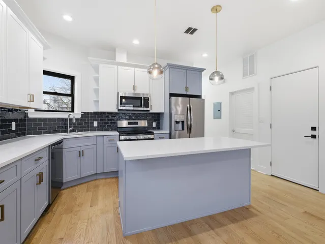 a large kitchen with stainless steel appliances a refrigerator a stove a sink dishwasher and white cabinets with wooden floor