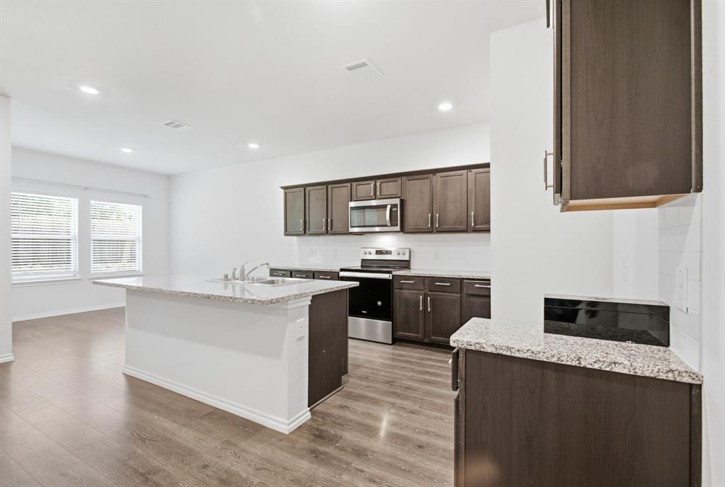 1328 Broaddus Road Forney, TX 75126 - Photo 12 of 31 Open-concept kitchen featuring an island with a double basin sink, granite countertops, wood-finish flooring, dark wood cabinetry, and stainless steel appliances