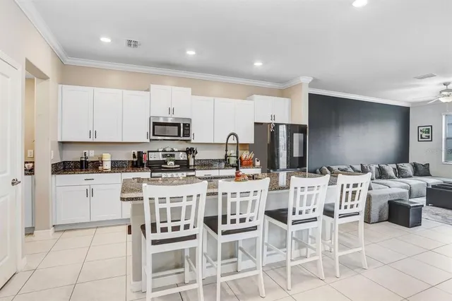 a kitchen with stainless steel appliances a stove a sink a refrigerator white cabinets and chairs