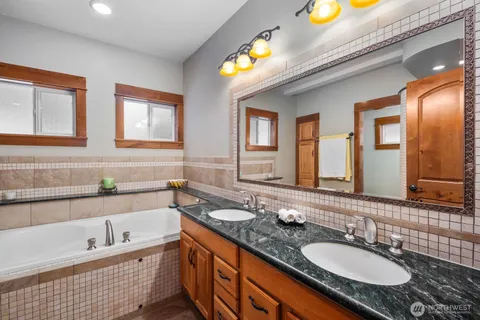 a bathroom with a granite countertop double vanity sink and a bathtub