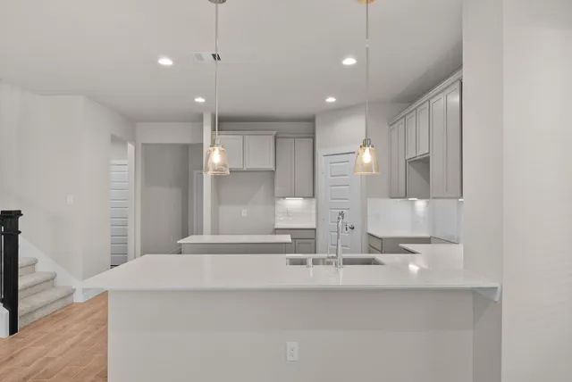 a view of an empty room with wooden floor and a kitchen
