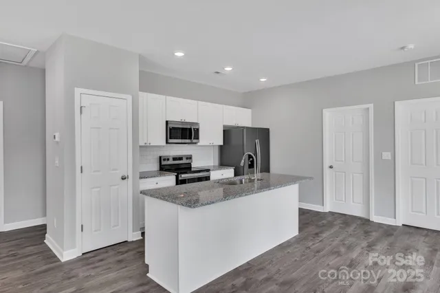 a kitchen with stainless steel appliances granite countertop a stove top oven a refrigerator a sink and dishwasher with wooden floor