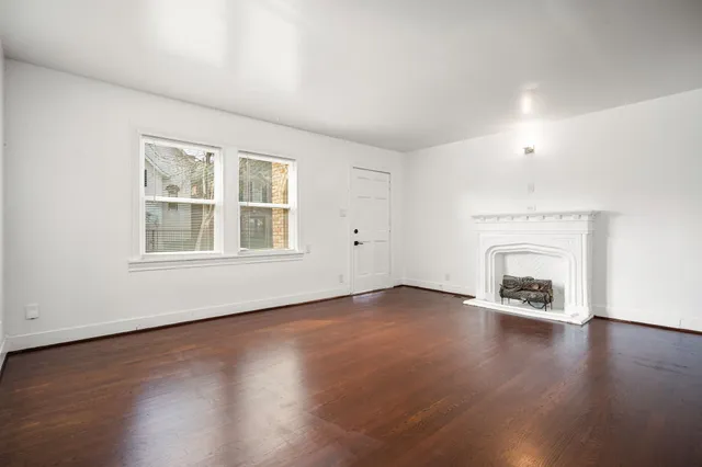 an empty room with wooden floor fireplace and windows