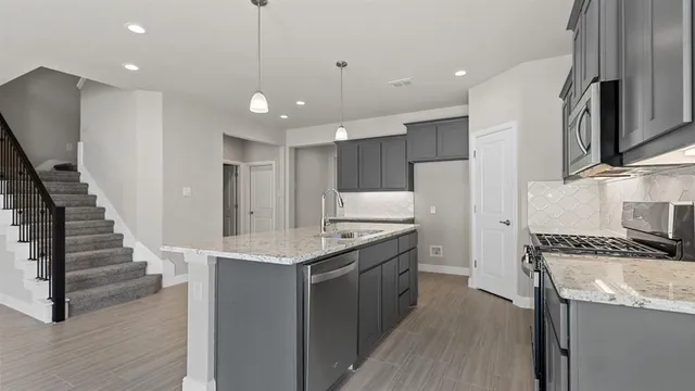 a kitchen with stainless steel appliances granite countertop a refrigerator a sink dishwasher a stove and white cabinets with wooden floor