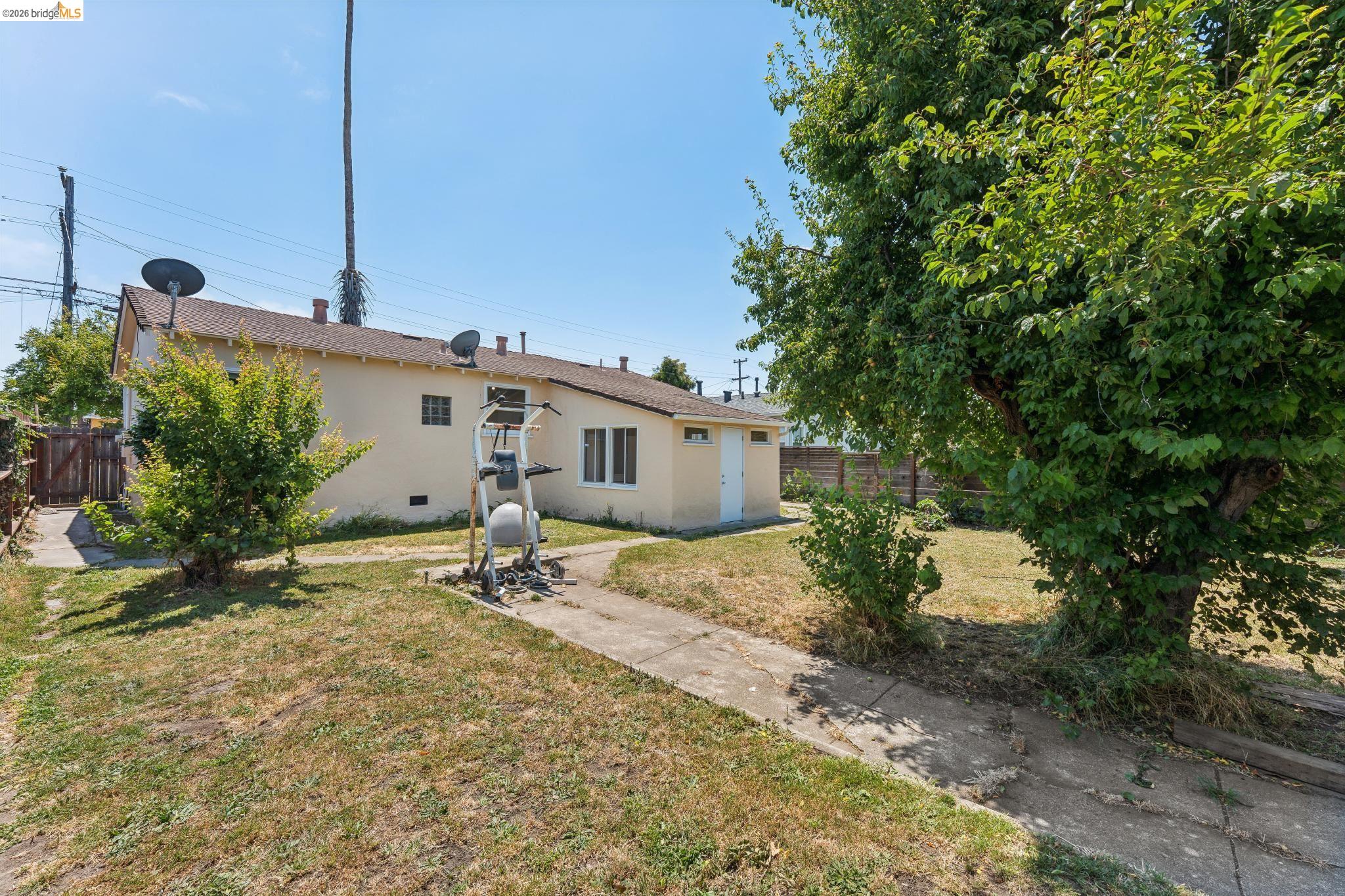 2879 Rheem Avenue Richmond, CA 94804 - Photo 40 of 45 Expansive rear yard featuring a concrete pathway, mature trees, and a light-colored exterior building with multiple windows