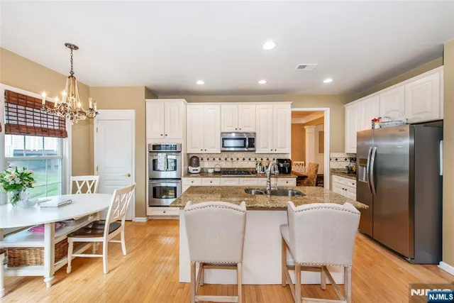 a kitchen with stainless steel appliances granite countertop a refrigerator a stove top oven a sink dishwasher and a dining table with wooden floor