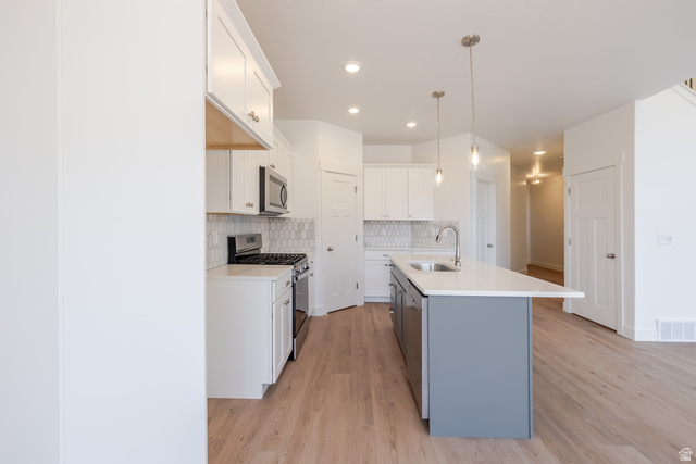 5228 South Acacia Drive, Unit 808 Mapleton, UT 84664 - Photo 10 of 22 Spacious kitchen featuring white cabinetry, light wood-finish flooring, a stainless steel gas range, a patterned tile backsplash, and a two-tone island with an undermount sink