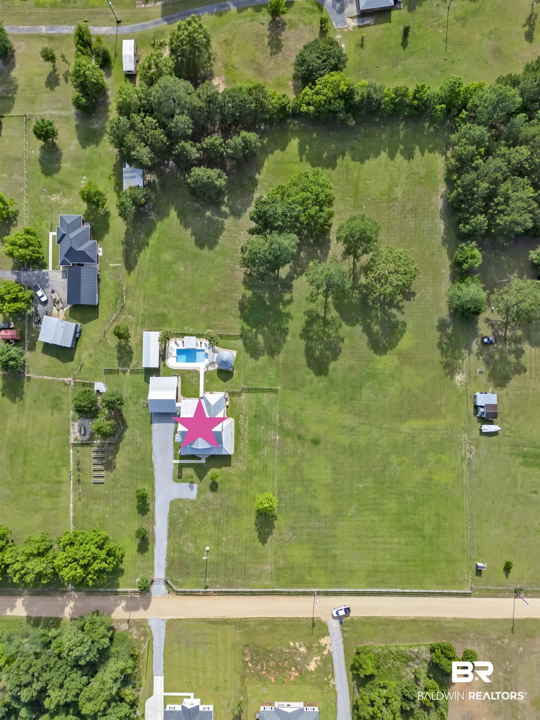 6576 Ranch Loop Road East Grand Bay, AL 36541 - Photo 37 of 39 Expansive property featuring a central residence with a distinctive pink star roof accent, a rectangular swimming pool with a surrounding patio, a lengthy gravel driveway, and multiple mature trees