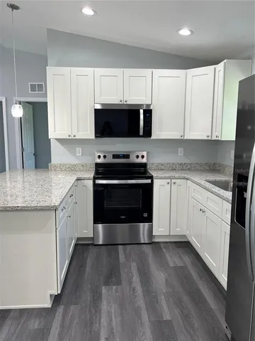 a kitchen with stainless steel appliances granite countertop a stove top oven a sink dishwasher and a refrigerator with wooden floor