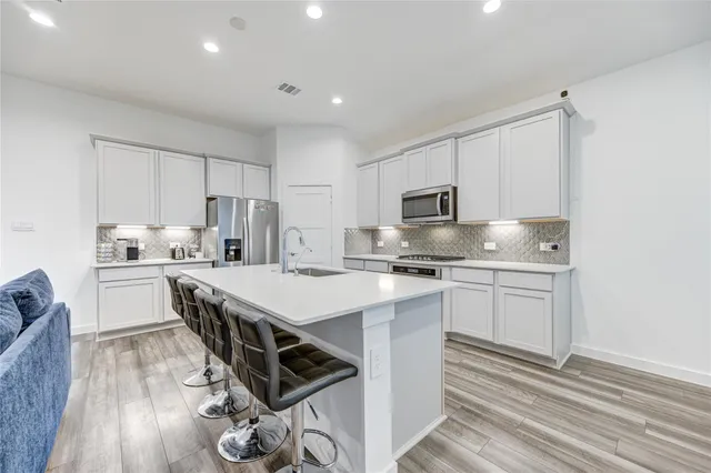 a kitchen with stainless steel appliances a stove top oven a sink dishwasher and a refrigerator with wooden floor