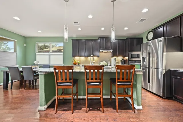a kitchen with stainless steel appliances kitchen island granite countertop a dining table chairs refrigerator and sink