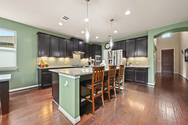 a kitchen with stainless steel appliances kitchen island granite countertop a table chairs and a refrigerator