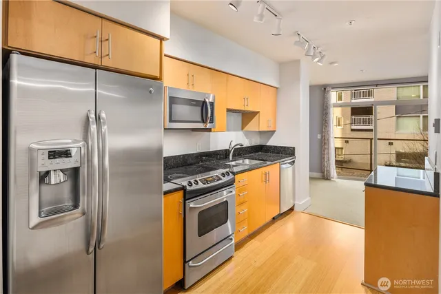 a kitchen with stainless steel appliances granite countertop a refrigerator a stove and a sink with wooden floor