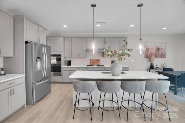 a kitchen with stainless steel appliances kitchen island granite countertop a dining table chairs sink and cabinets