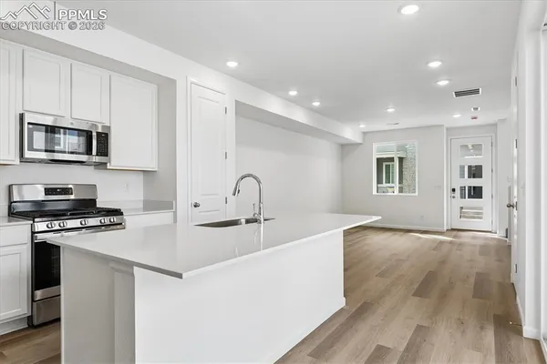 a kitchen with stainless steel appliances granite countertop a stove top oven a sink a refrigerator white cabinets and couches with wooden floor