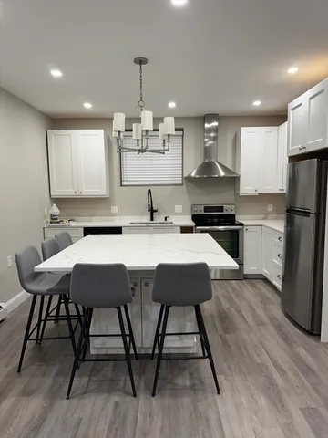 a kitchen with stainless steel appliances kitchen island granite countertop a sink a stove a refrigerator and a dining table with wooden floor