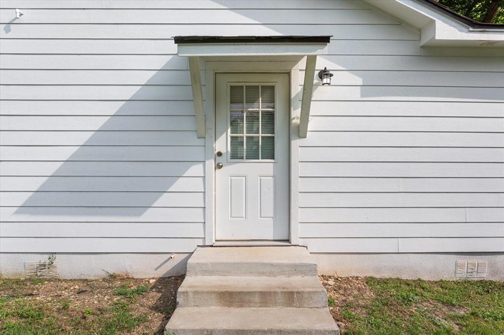 3109 North 20th Street Waco, TX 76708 - Photo 20 of 24 White exterior siding with a covered entry door, featuring a window panel and an exterior light fixture