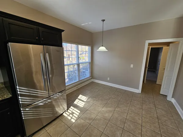 a view of a refrigerator in kitchen and an empty room with wooden floor
