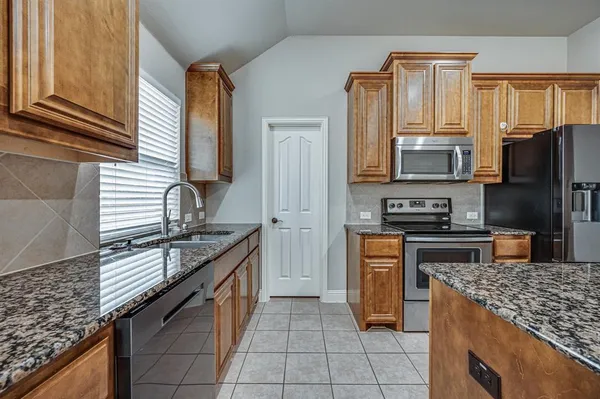 a kitchen with stainless steel appliances granite countertop a stove top oven a sink dishwasher and a refrigerator with wooden cabinets