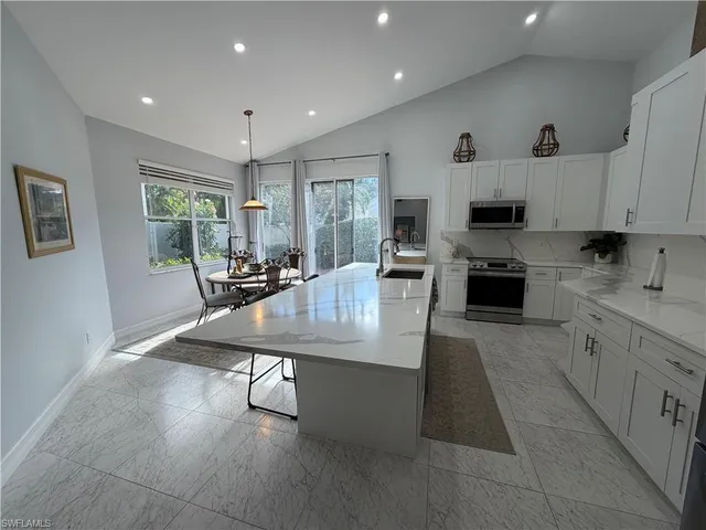 a living room with stainless steel appliances furniture a rug kitchen view and a window