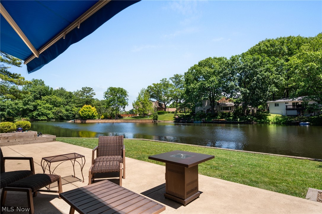 685 Sunnyside Road Vermilion, OH 44089 - Photo 2 of 50 Spacious concrete patio featuring a retractable blue awning, a lush green lawn, and direct waterfront access