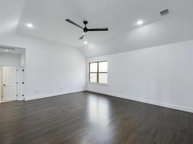 an empty room with wooden floor ceiling fan and windows