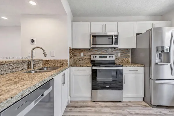 a kitchen with granite countertop a sink stainless steel appliances and white cabinets