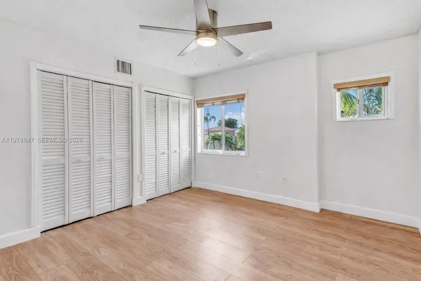 an empty room with wooden floor chandelier fan and windows