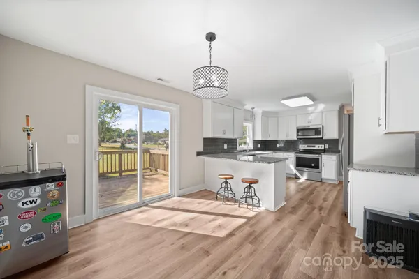 a open kitchen with stainless steel appliances granite countertop a stove a refrigerator a sink dishwasher and white cabinets with wooden floor