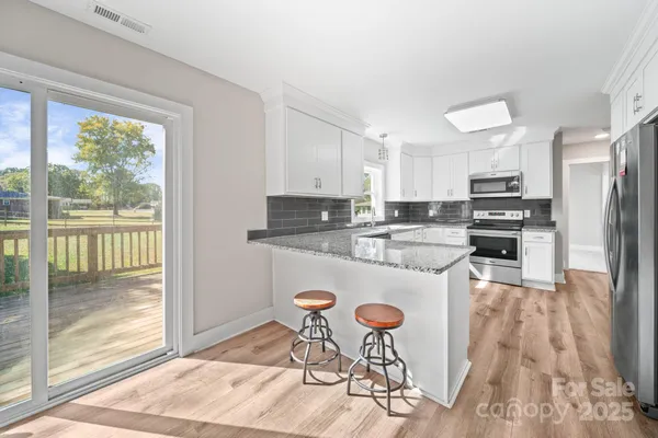 a kitchen with granite countertop a stove a refrigerator and white cabinets with wooden floors